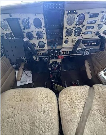 A wide view of the aircraft cockpit showing the instrument panel and two front seats with sheepskin covers.