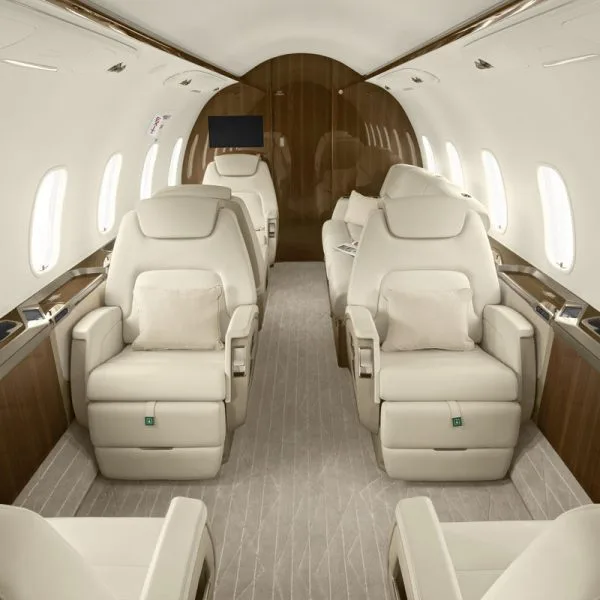 The luxurious interior cabin of a private jet with cream leather seats and wood paneling.