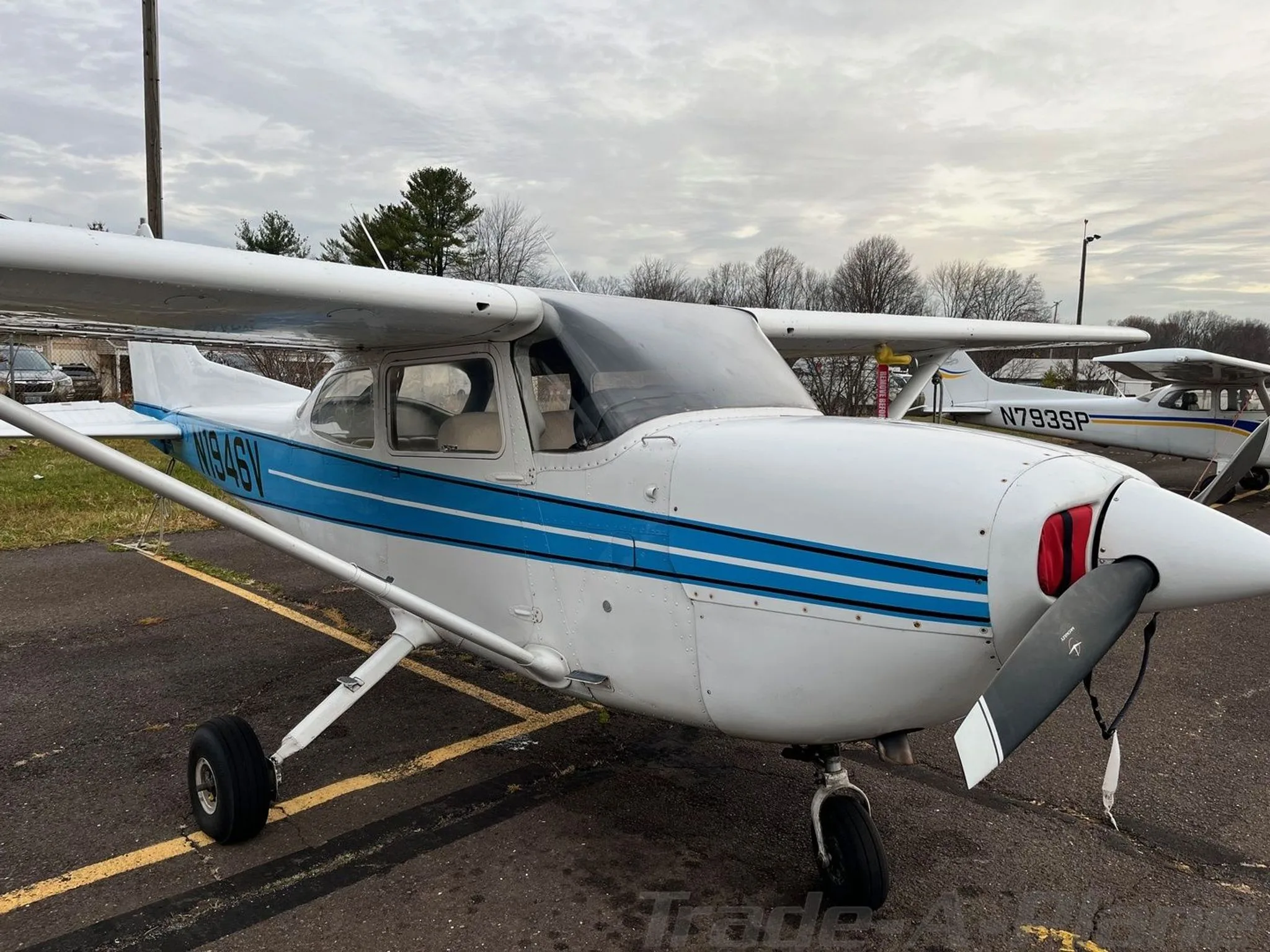 A front-quarter view of the N1946V aircraft, a white plane with blue stripes, parked on an airfield.