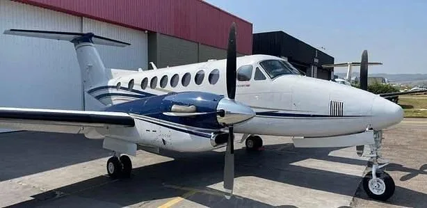 A white and blue twin-engine turboprop aircraft parked on an airfield next to a hangar.