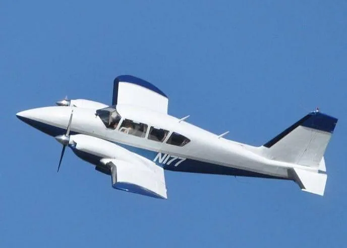 A white and blue twin-engine aircraft, registration N177, flies against a clear blue sky.
