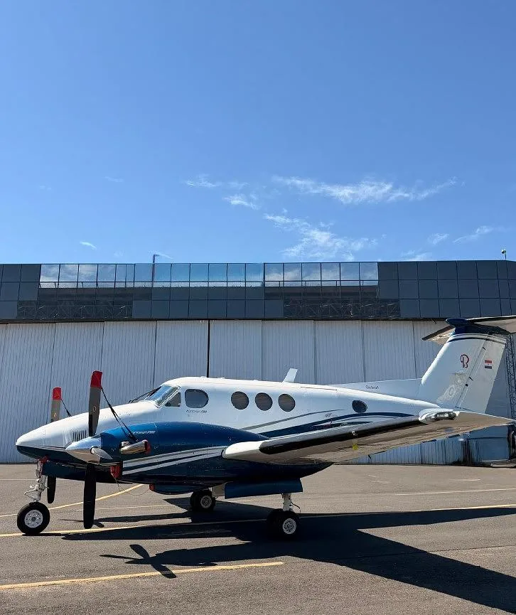 A Beechcraft King Air with blue and white livery, registration ZP-JYA, parked on a tarmac with its propellers visible.