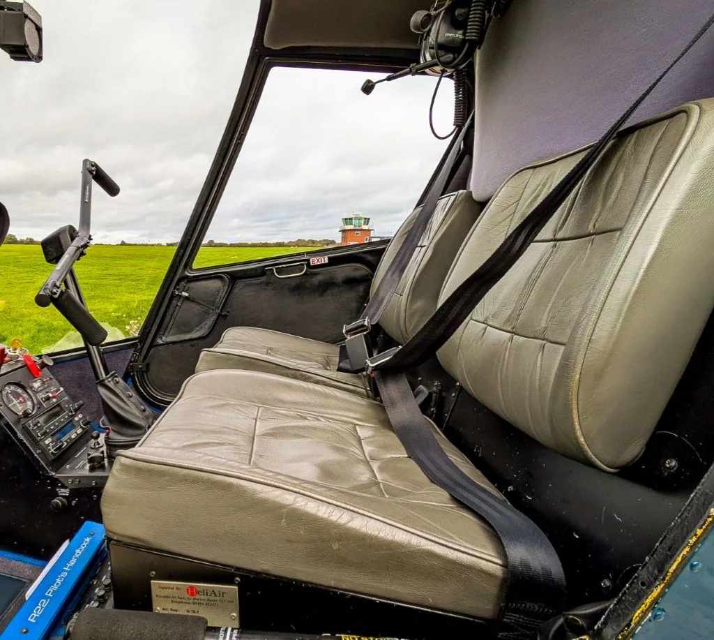 The grey leather seats and interior cabin of a helicopter, with a control tower visible through the window.