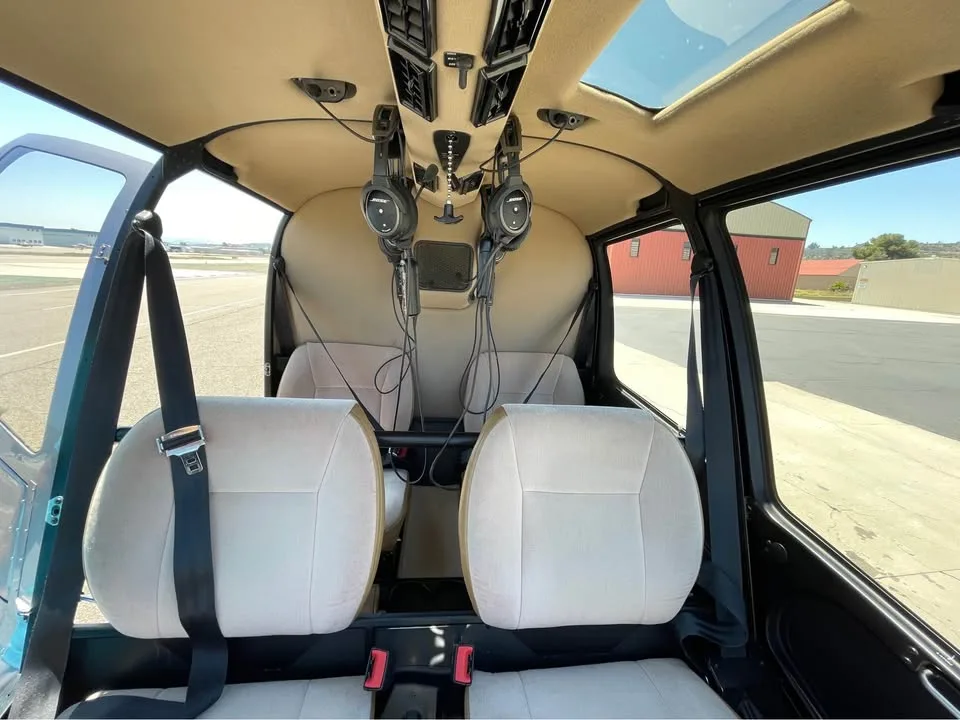 The beige interior cabin of a Robinson R44 helicopter with two headsets hanging from the ceiling.