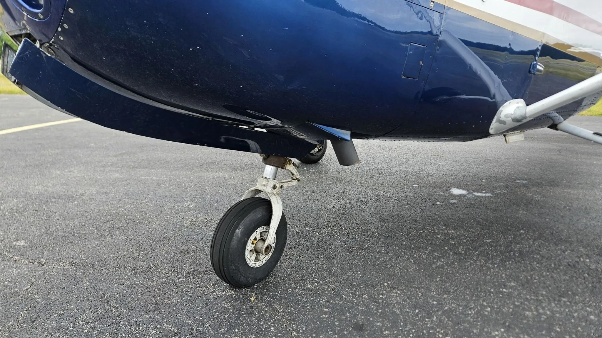 A close-up view of the front landing gear and lower fuselage of the blue and white Cessna 182.