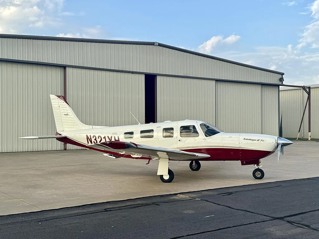 A white and maroon Piper Saratoga II TC aircraft (N321YH) parked on an airport apron in front of a large hangar.