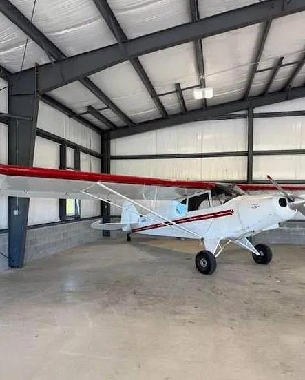 A white aircraft with red wings and stripes parked inside a metal hangar.