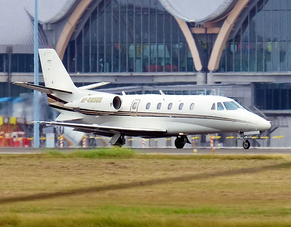 A white business jet with gold and black stripes on a runway, with a modern airport terminal in the background.