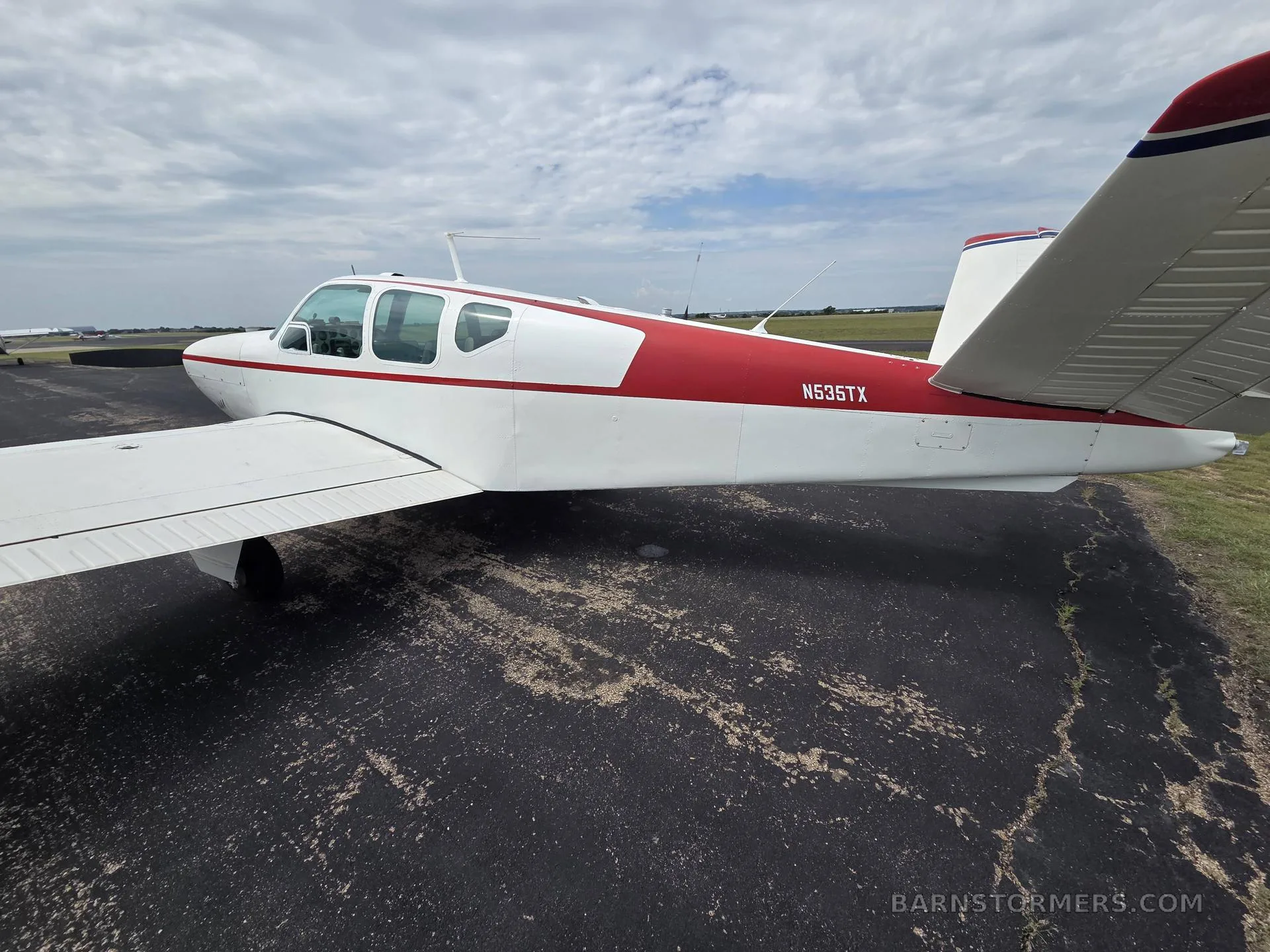 A white and red Beechcraft Bonanza aircraft with registration N535TX is parked on an asphalt ramp, viewed from the left rear.