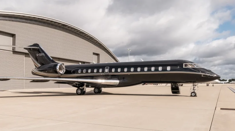 A black Bombardier Global business jet with gold accents parked on an airfield next to a modern hangar.