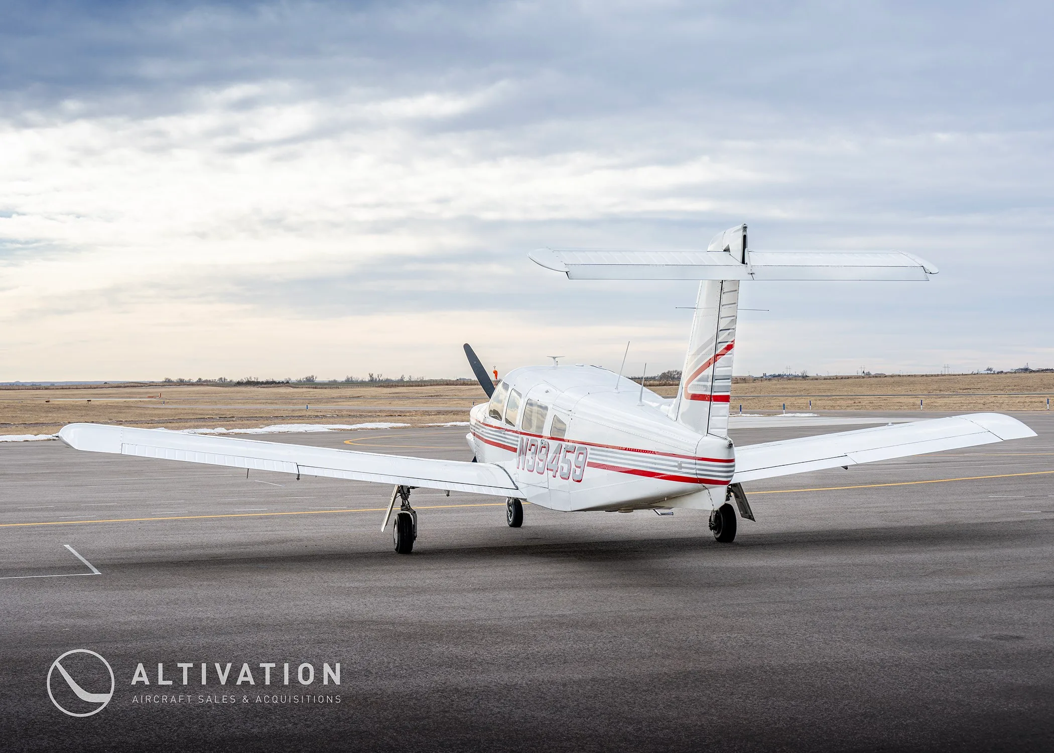 A white single-engine propeller aircraft with red and grey stripes, tail number N39459, seen from the rear on an airfield.