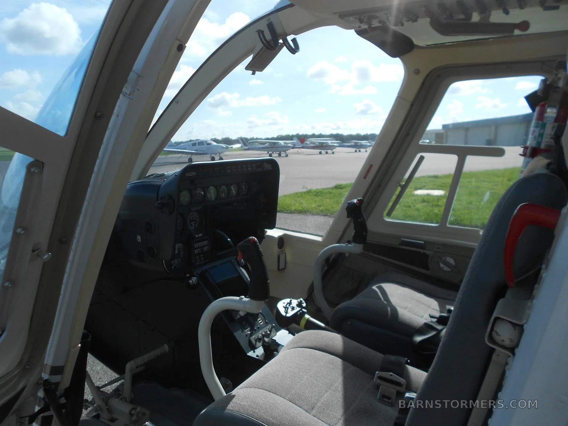 View from inside the helicopter cabin looking forward at the cockpit and other aircraft parked on the tarmac outside.
