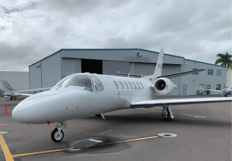 A white Cessna Citation business jet (N768JS) is parked on an airport tarmac next to a hangar.