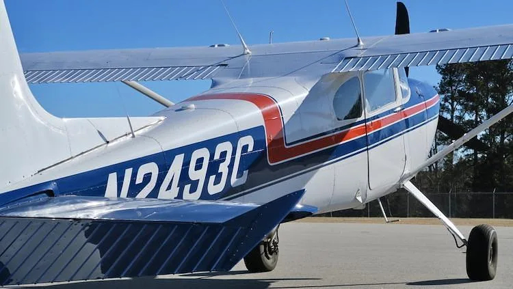 A close-up of the tail section of a white and blue Cessna 180 Skywagon, showing the N2493C registration and red stripe.