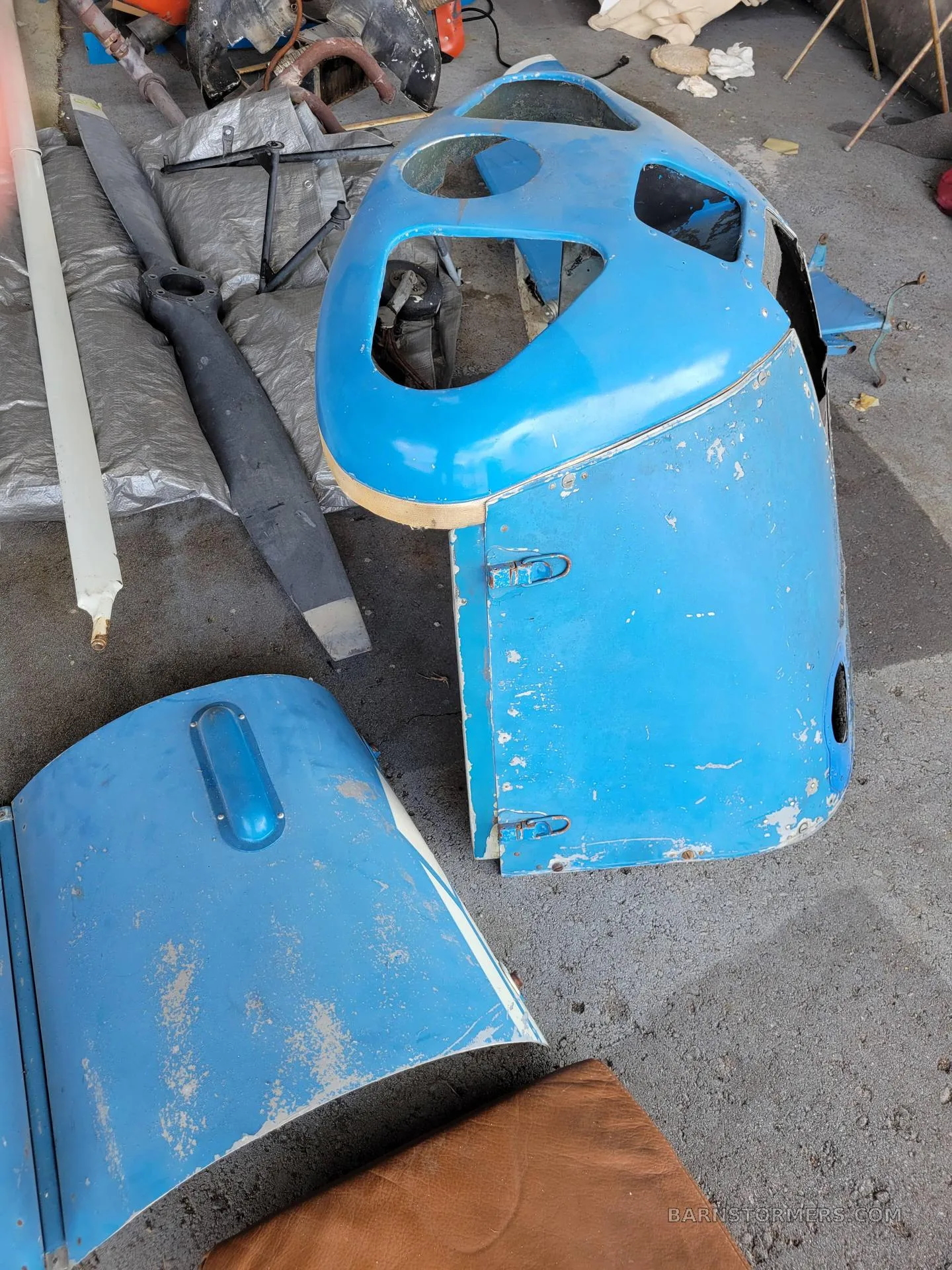 Disassembled blue aircraft cowling parts and a propeller lying on a concrete floor.