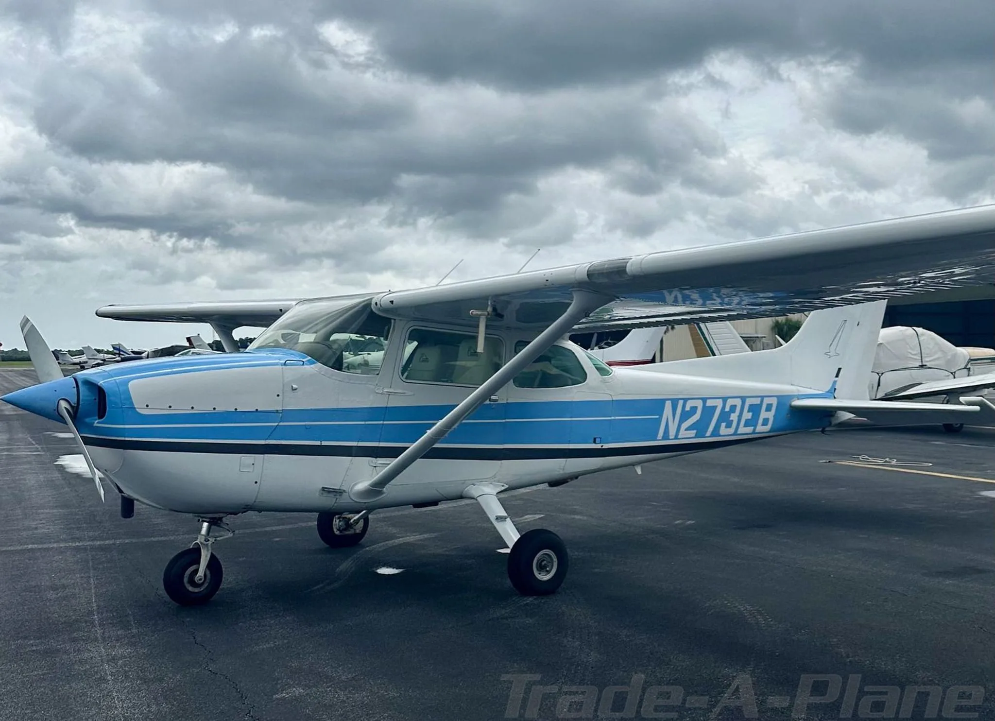A front-side view of the white and blue Cessna 172, registration N273EB, parked on an airport ramp.