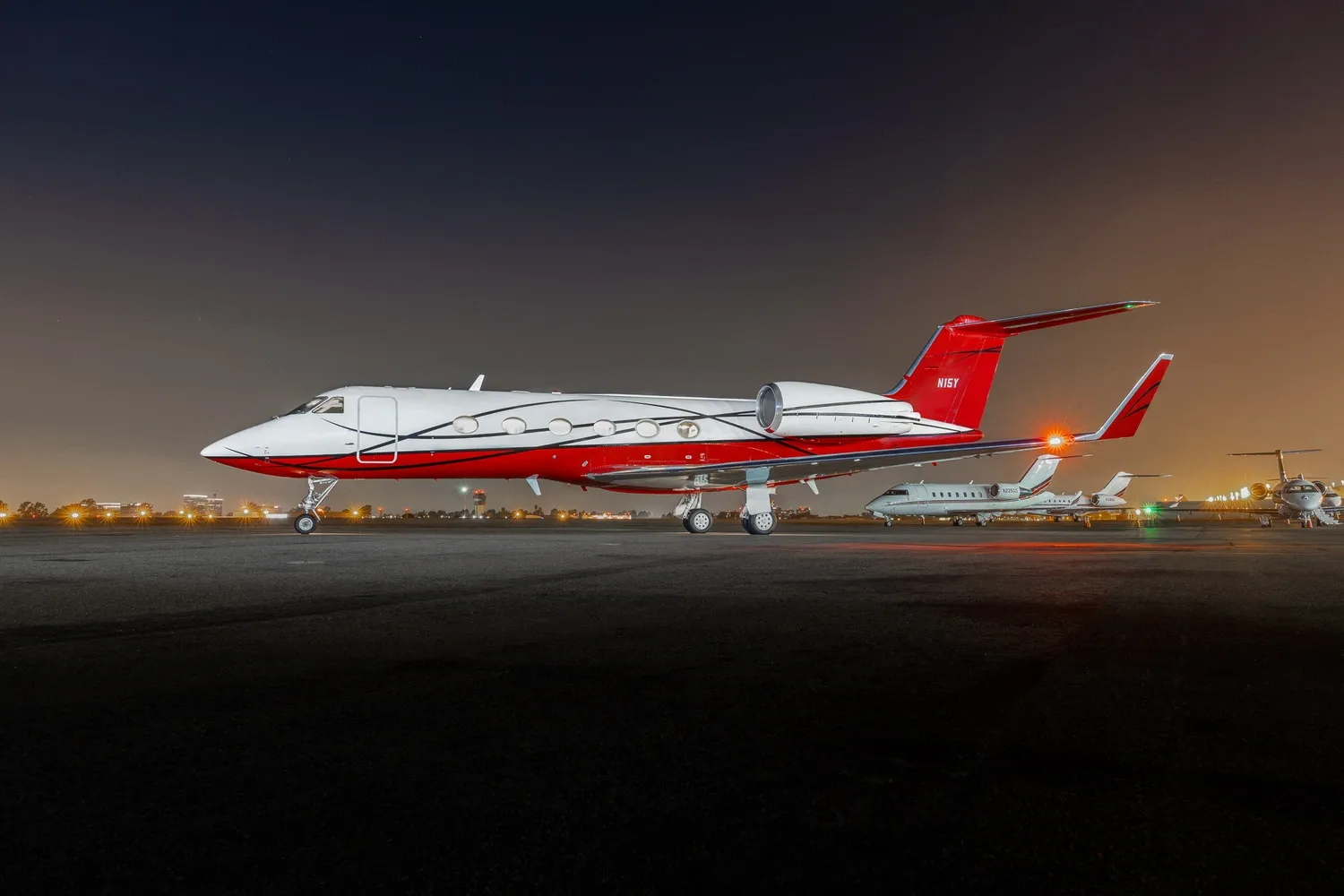 A red and white Gulfstream jet with black accents is parked on an airport tarmac at night.