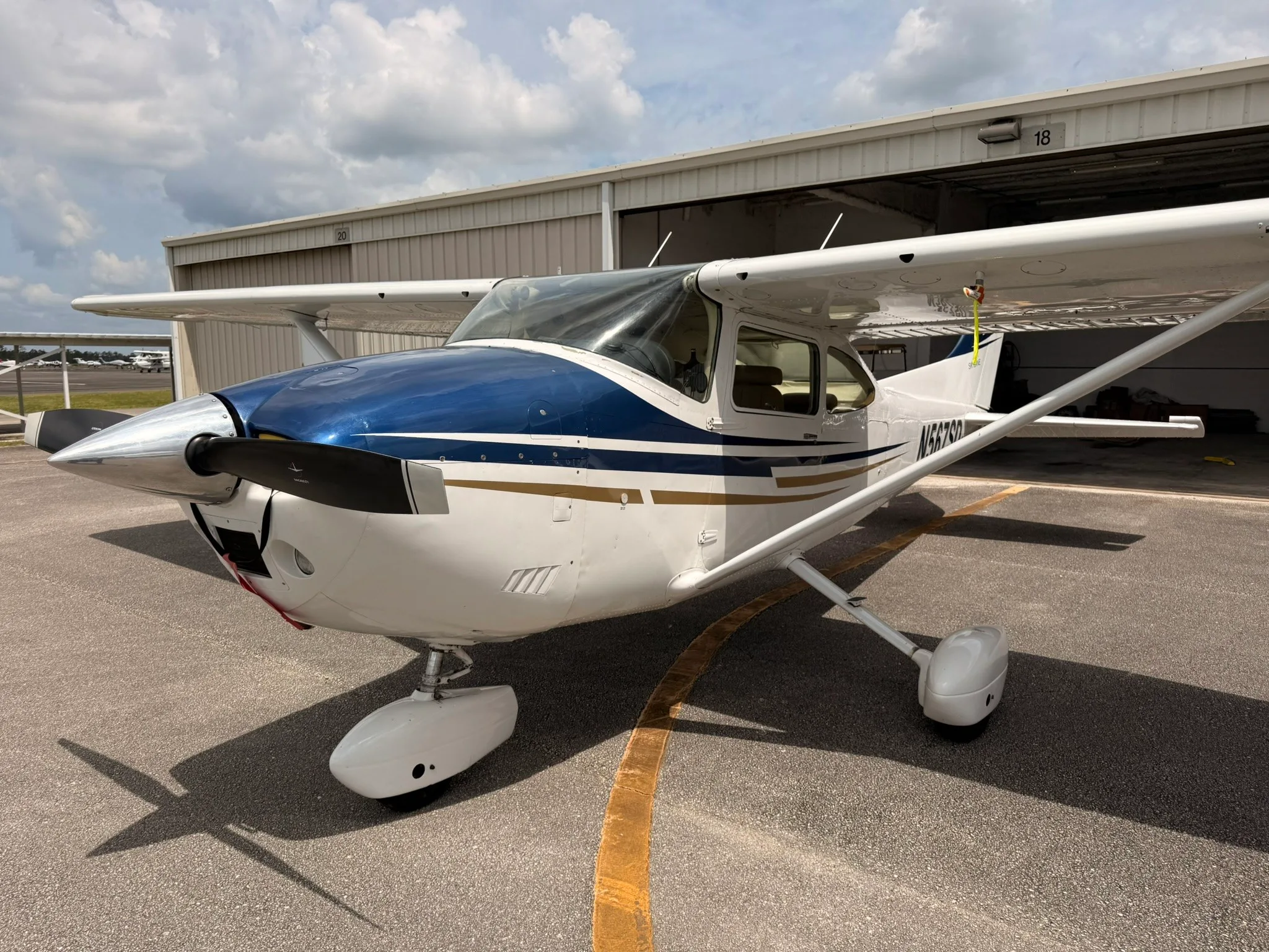 A front-left view of the Cessna Skylane N567SD showing its propeller and nose cone, parked near a hangar.