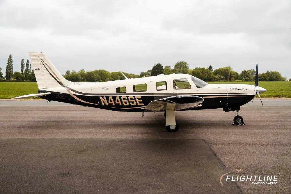 A side profile of a white and black Piper Saratoga II TC, registration N446SE, parked on an asphalt runway.