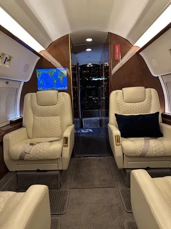 Two cream-colored quilted leather seats face each other in the private jet's cabin, with a world map displayed on a screen.