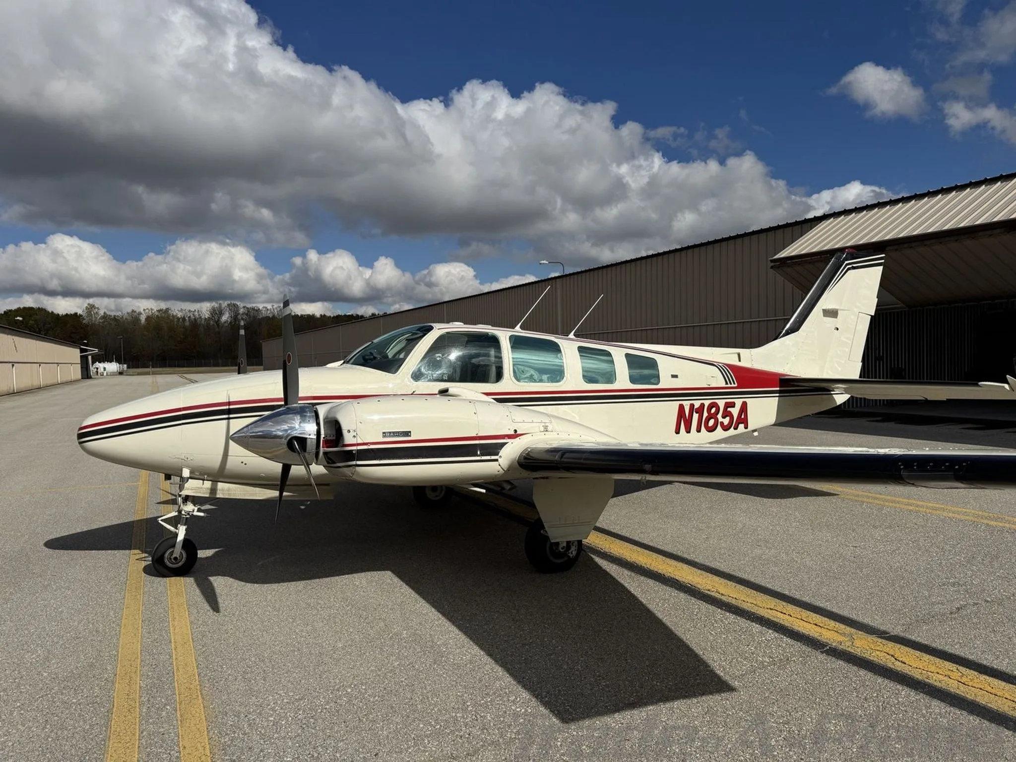 A side-front view of the N185A twin-engine aircraft, white with red and black stripes, parked on an airport tarmac.