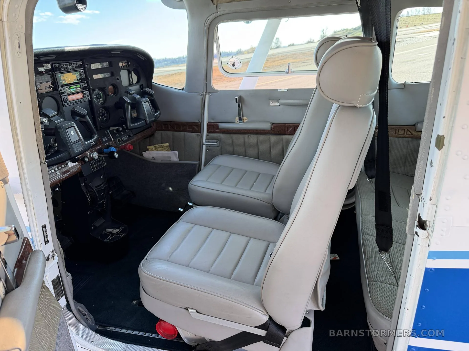 The interior of a Cessna aircraft, showing the light gray front seats and a partial view of the cockpit.