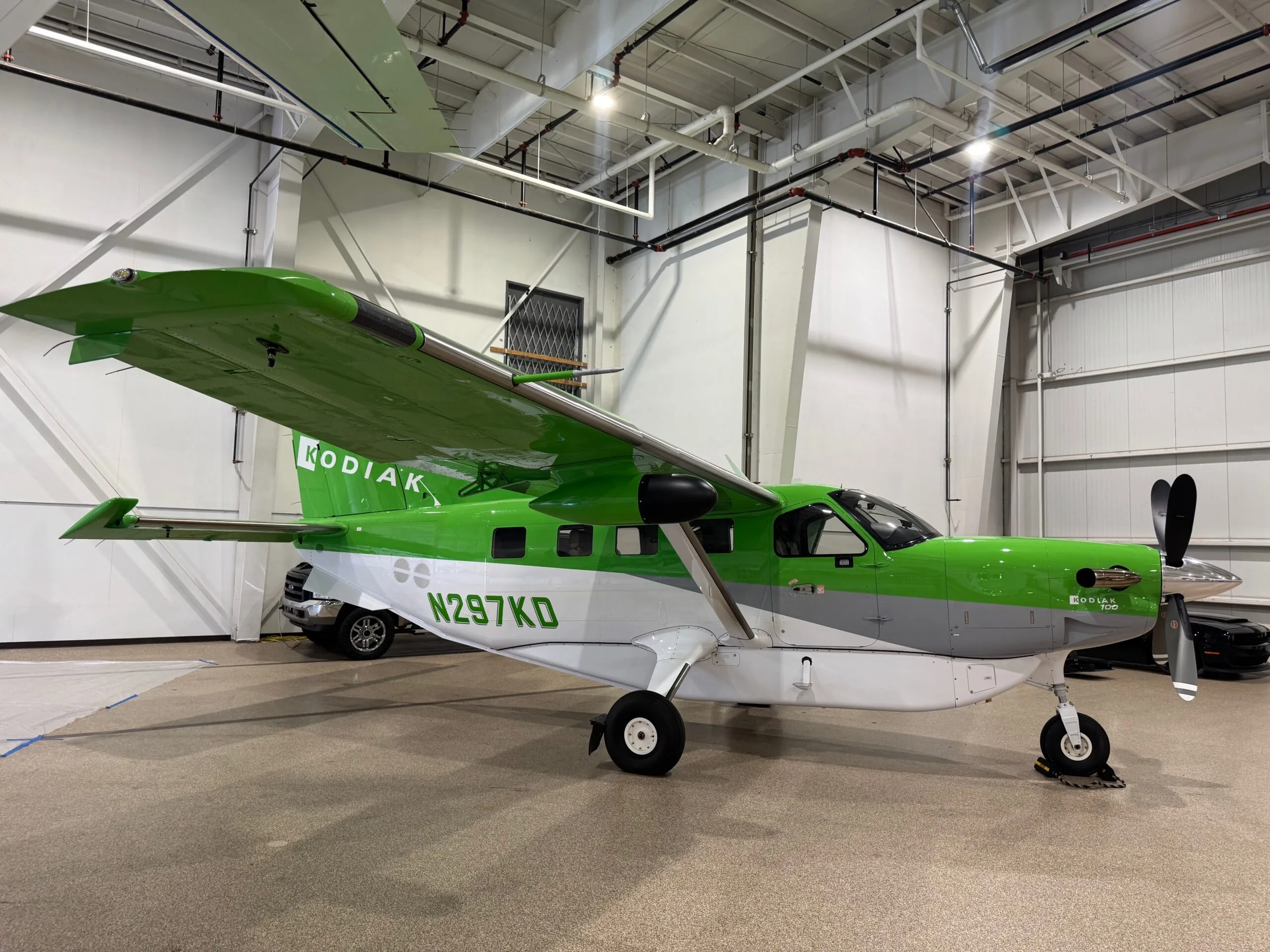 A green, white, and grey Kodiak aircraft (N297KD) parked inside a hangar.