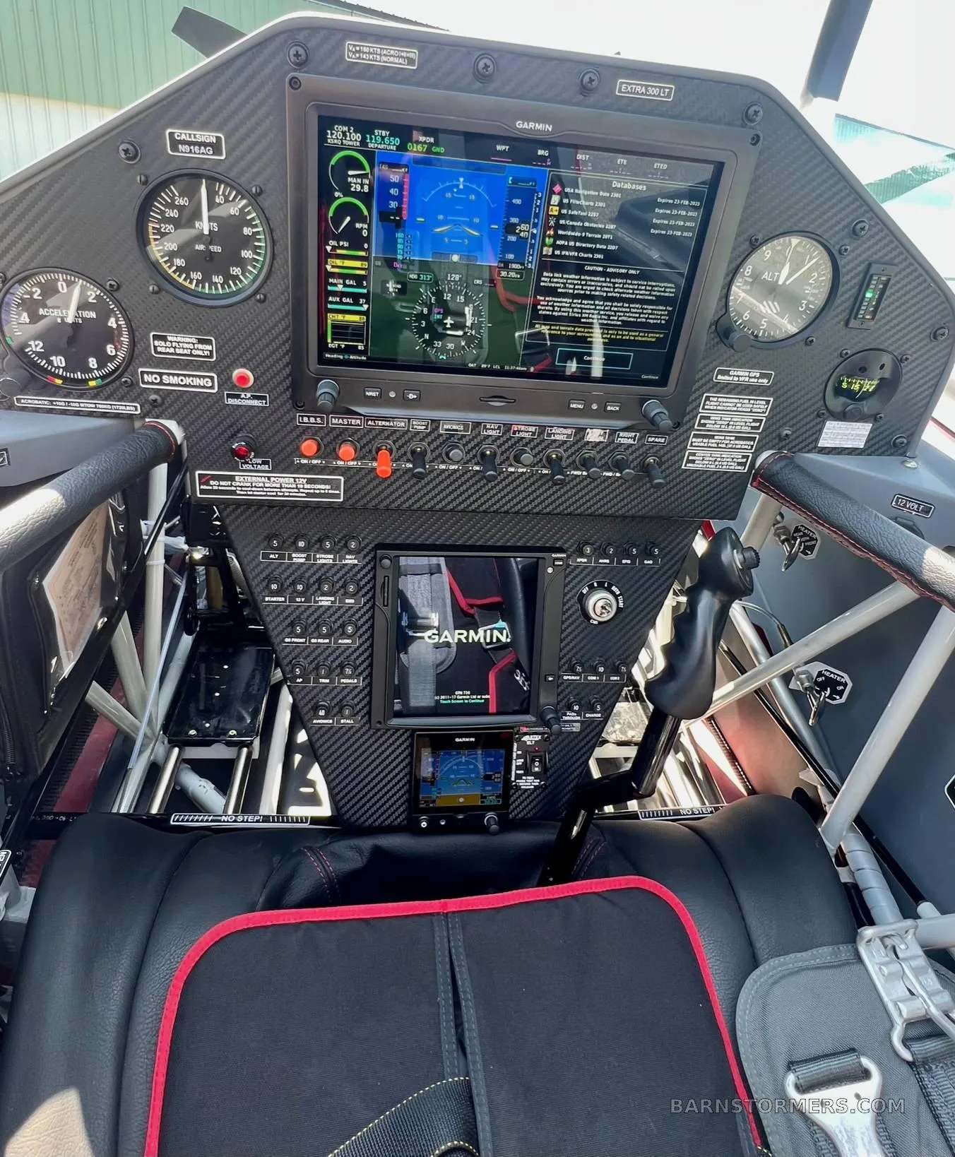 The cockpit of an aerobatic aircraft features a modern glass panel display, traditional gauges, and a carbon fiber instrument panel.