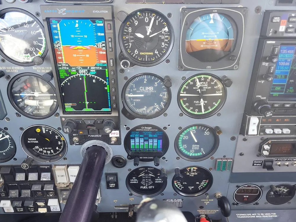 A detailed view of a Piper PA-46-350P Malibu Mirage cockpit instrument panel, featuring both analog gauges and a modern digital display.