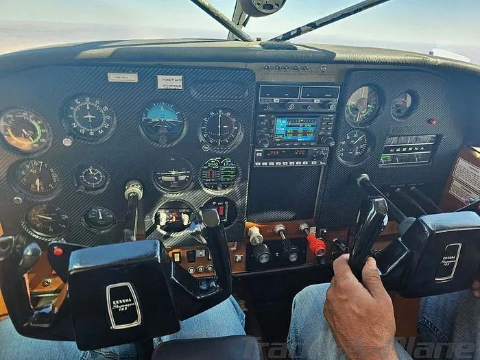 The cockpit of a Cessna aircraft with a black instrument panel, dual yokes, and a pilot's hands on the controls.