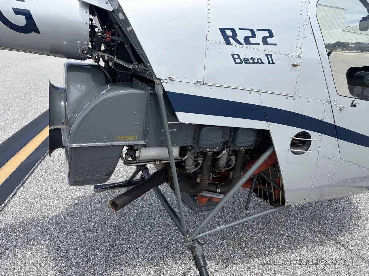 A close-up view of the exposed engine and mechanical components of a silver Robinson R22 Beta II helicopter.
