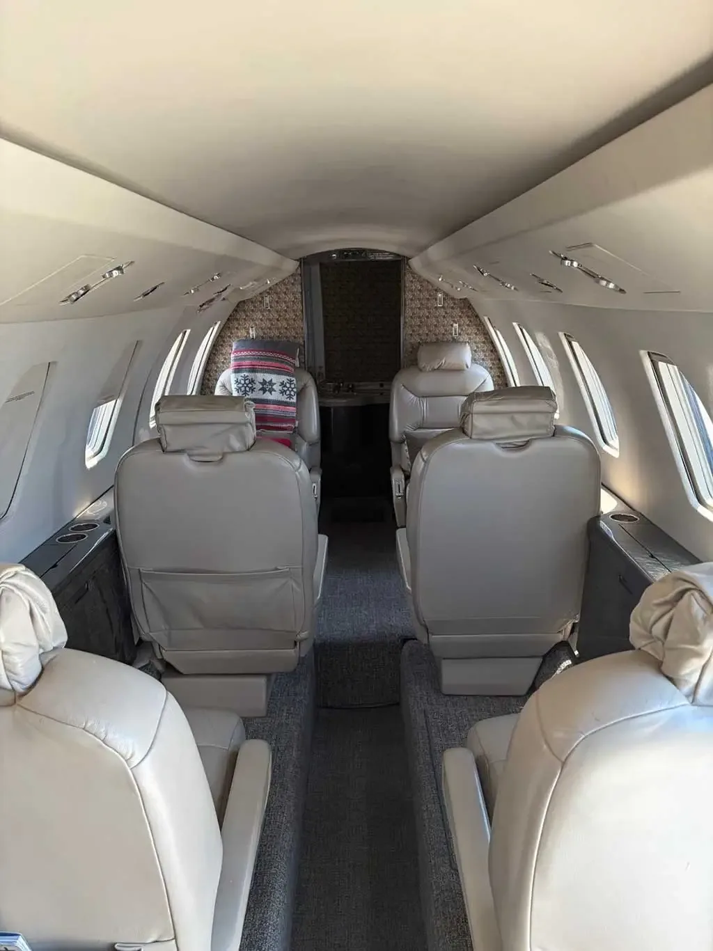 The interior cabin of a private jet, looking towards the front, with beige leather seats and a patterned blanket on a seat.