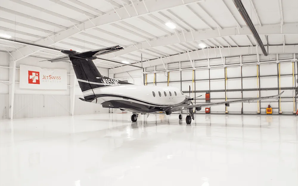 Rear view of a black and white Pilatus PC-12 turboprop aircraft parked in a clean white hangar.