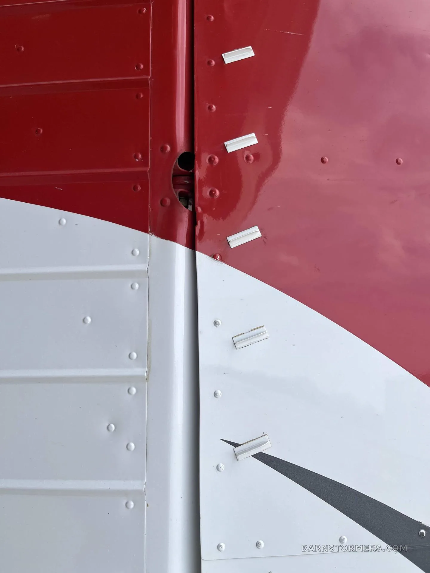 A close-up view of the red and white paint scheme and rivets on the fuselage of an aircraft.