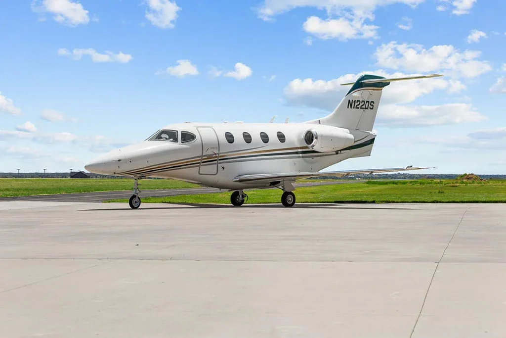 A white private jet with green and gold stripes and registration N122DS, parked on an airfield.