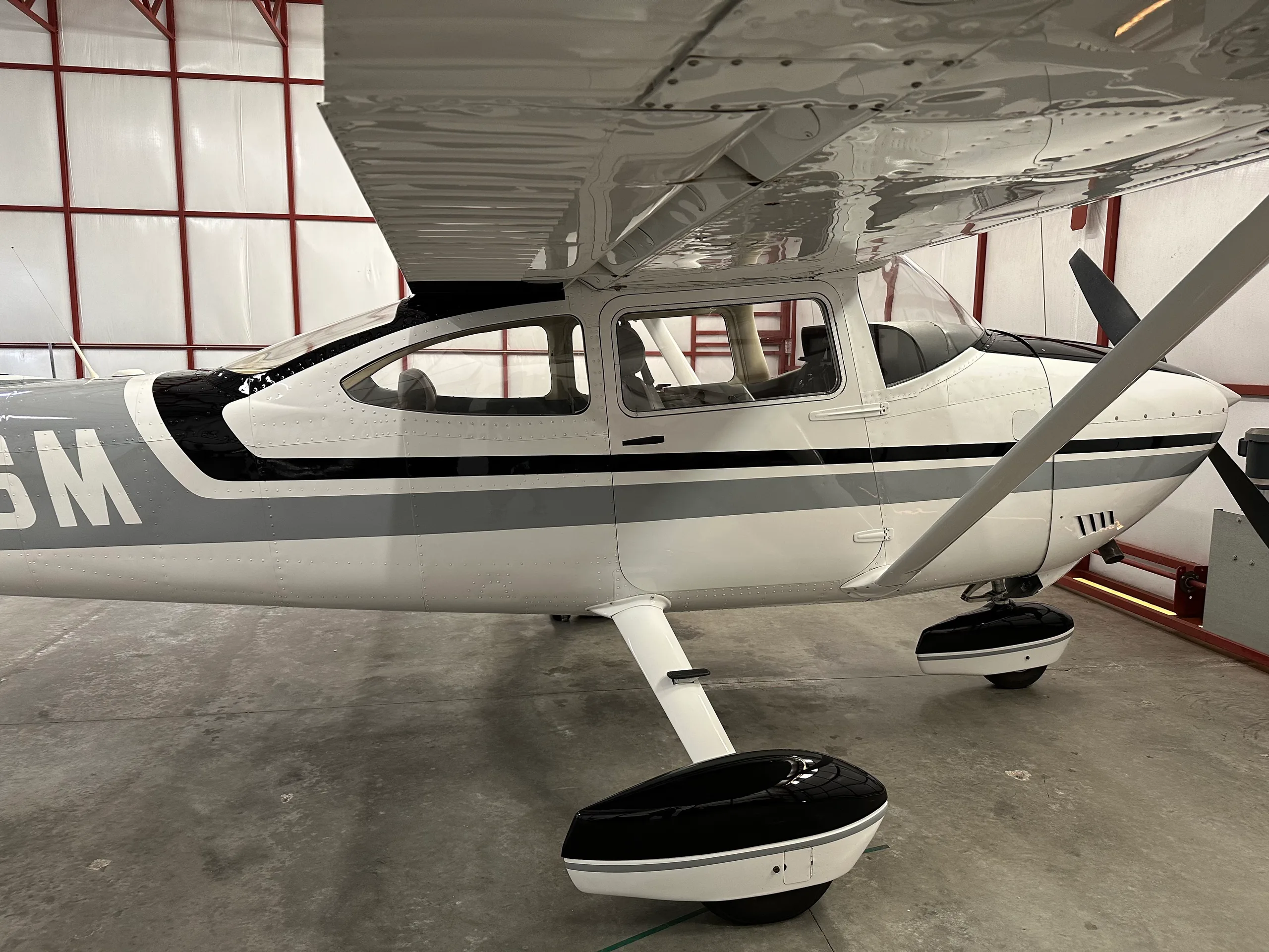 A side view of the Cessna 182 fuselage and wing, showing the black, grey, and white livery inside a hangar.