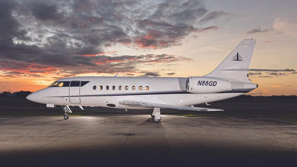 A white business jet, N88GD, with a dark blue stripe, parked on an tarmac at sunset.