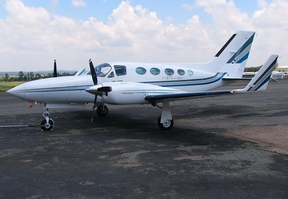 A white Cessna 421 Golden Eagle twin-engine aircraft with blue and grey stripes parked on an asphalt tarmac.