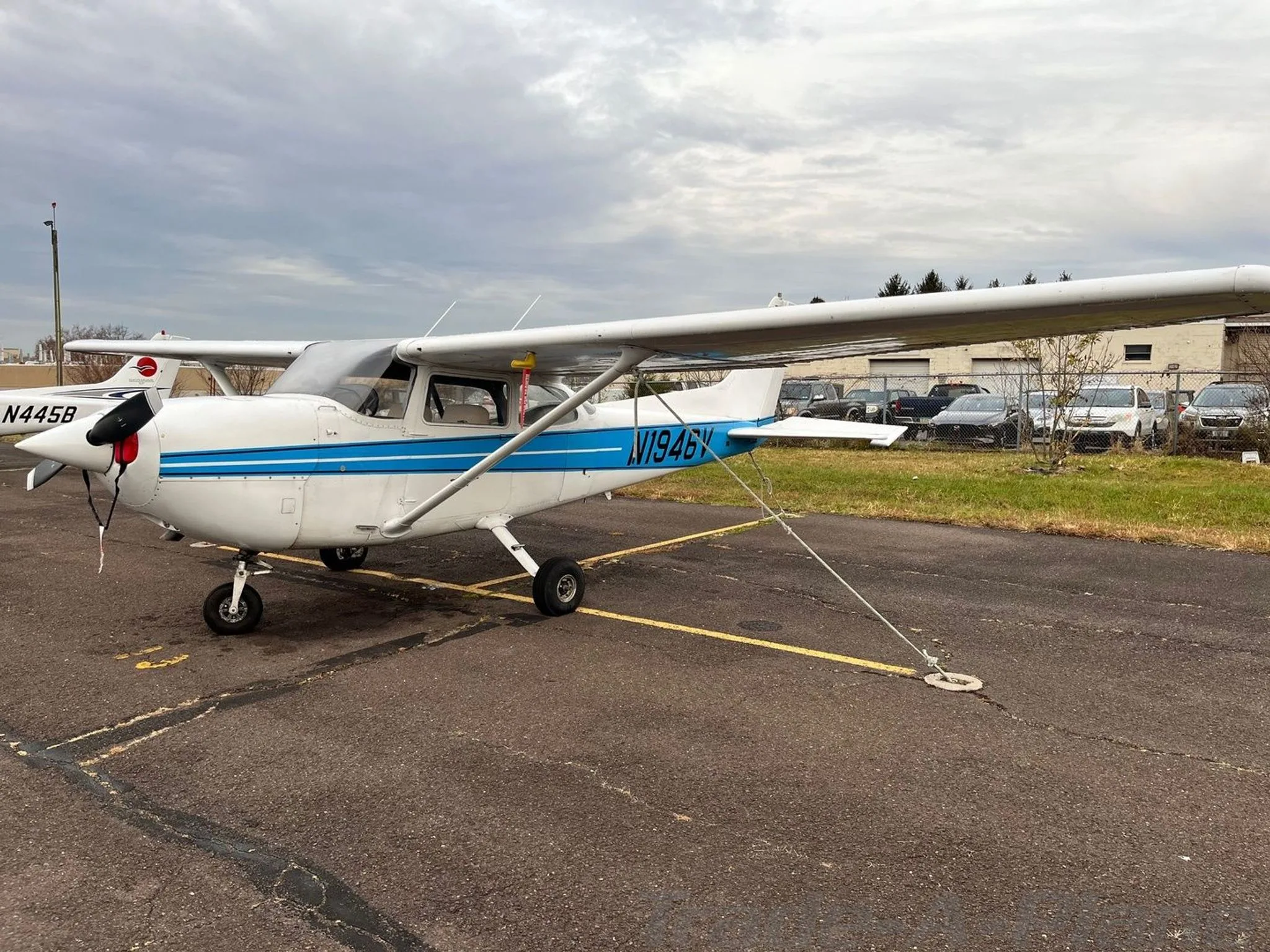 A white Cessna 172 with blue stripes, tail number N1946V, parked on an asphalt tarmac.