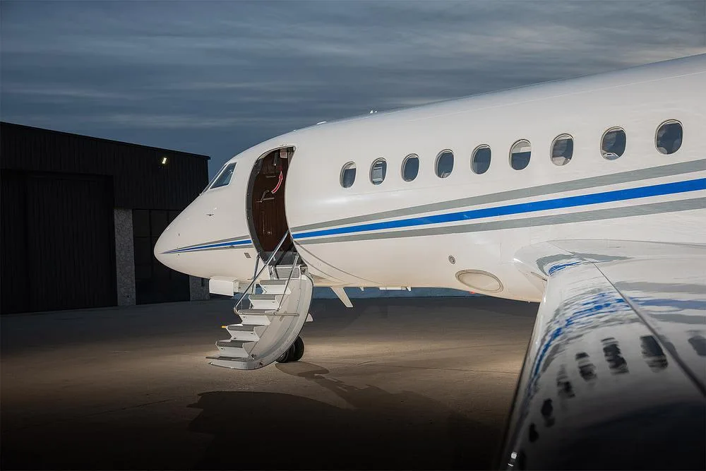 The front fuselage of a Dassault Falcon 900EX with its main entry door open and stairs deployed on the tarmac.