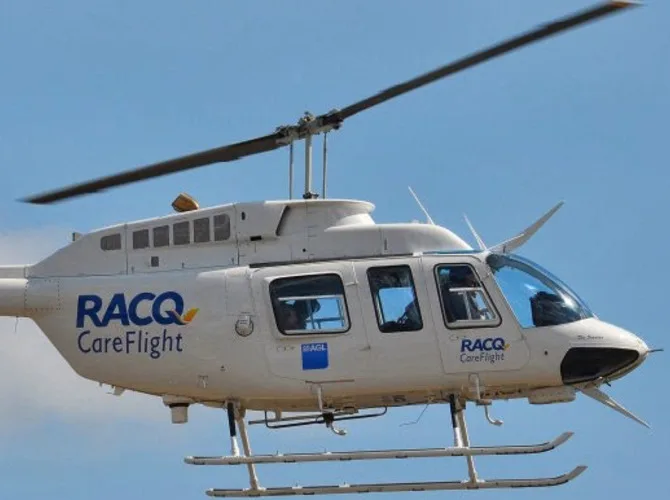 A white RACQ CareFlight helicopter with blue and orange logos flies against a clear blue sky.