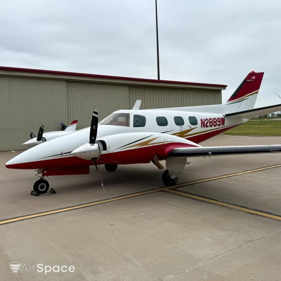 Side view of a white and red Beechcraft Duke N2889W parked on a tarmac next to a hangar.