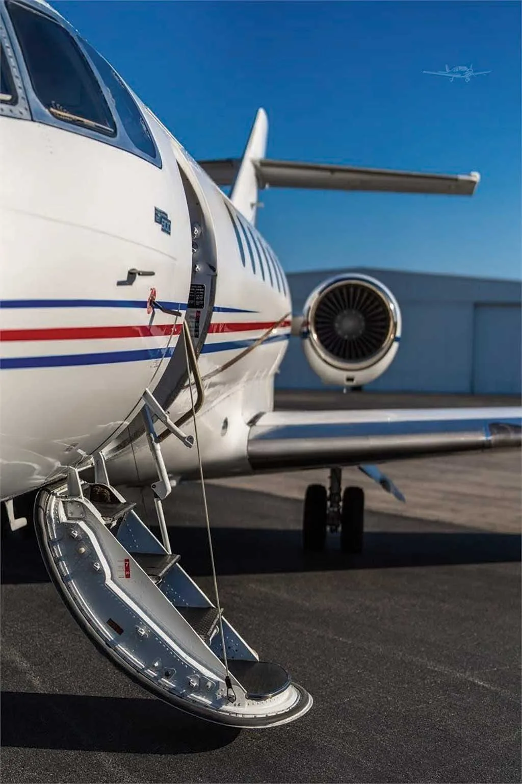 A close-up view of the open entry door and integrated airstairs of the white Dassault Falcon 50, N58BL, with its engine in the background.