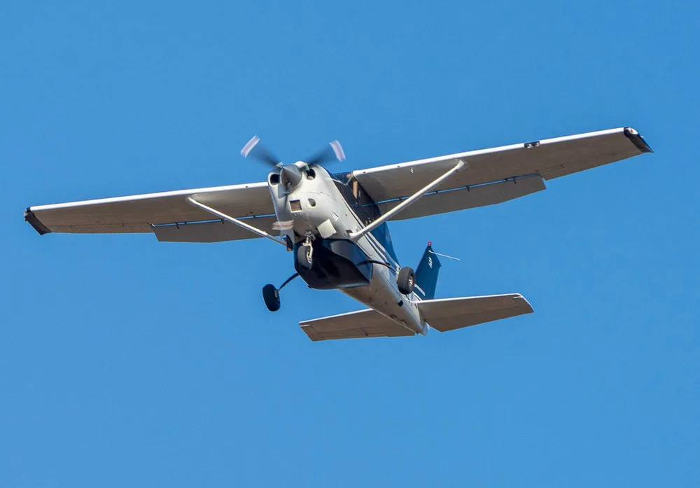 A white and black single-engine propeller aircraft is flying in a clear blue sky, viewed from below.