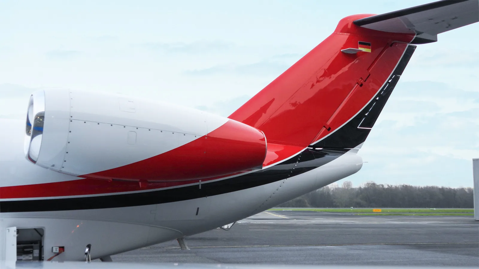 A close-up view of the red and black striped tail section of a Citation CJ4 business jet, featuring a German flag.