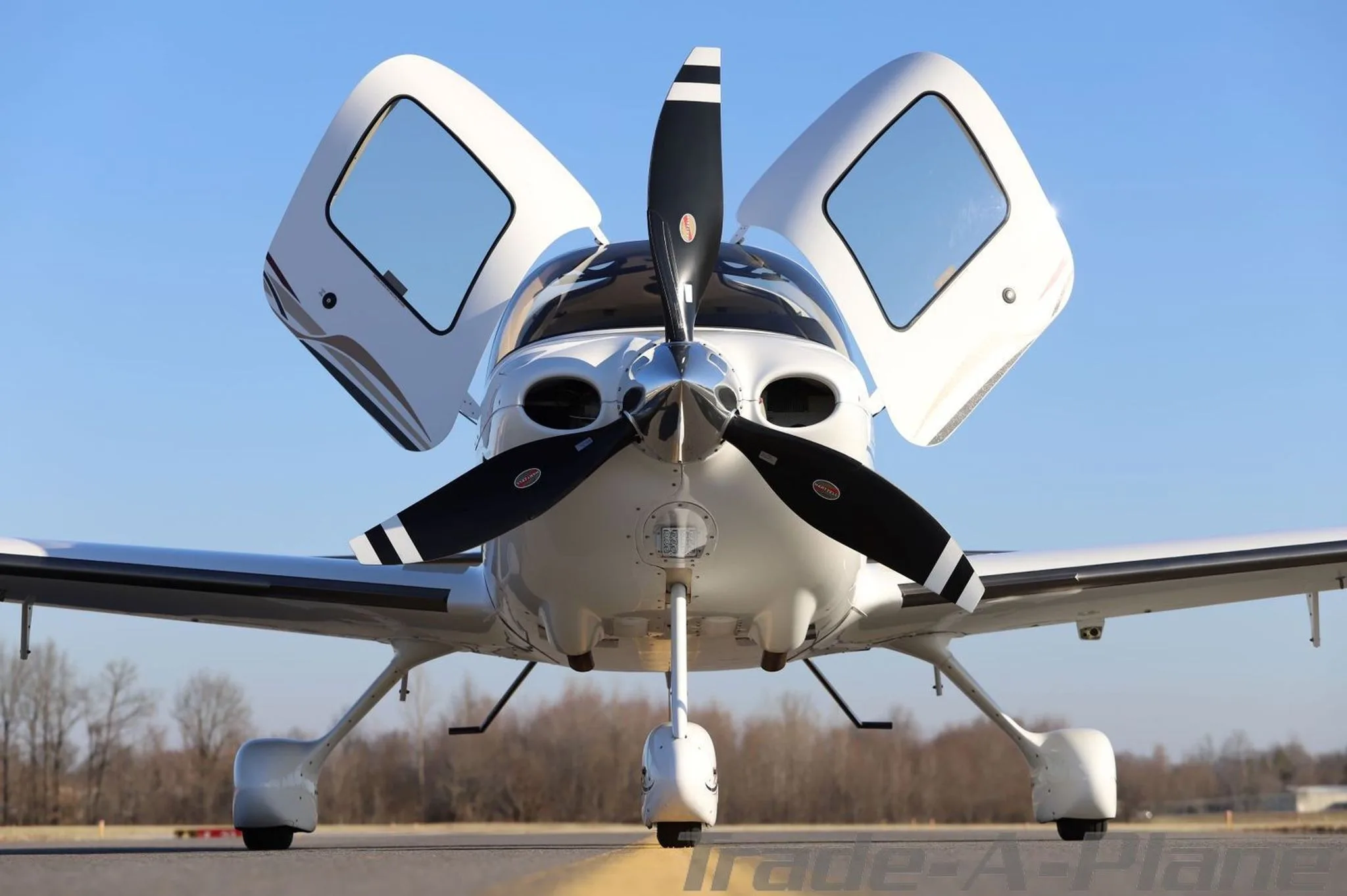 Front view of a white Cirrus SR22T aircraft with its doors open, parked on an airfield.