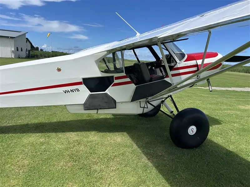 A side view of the white and red Super Cub with its door open, revealing the interior, parked on a grassy field.