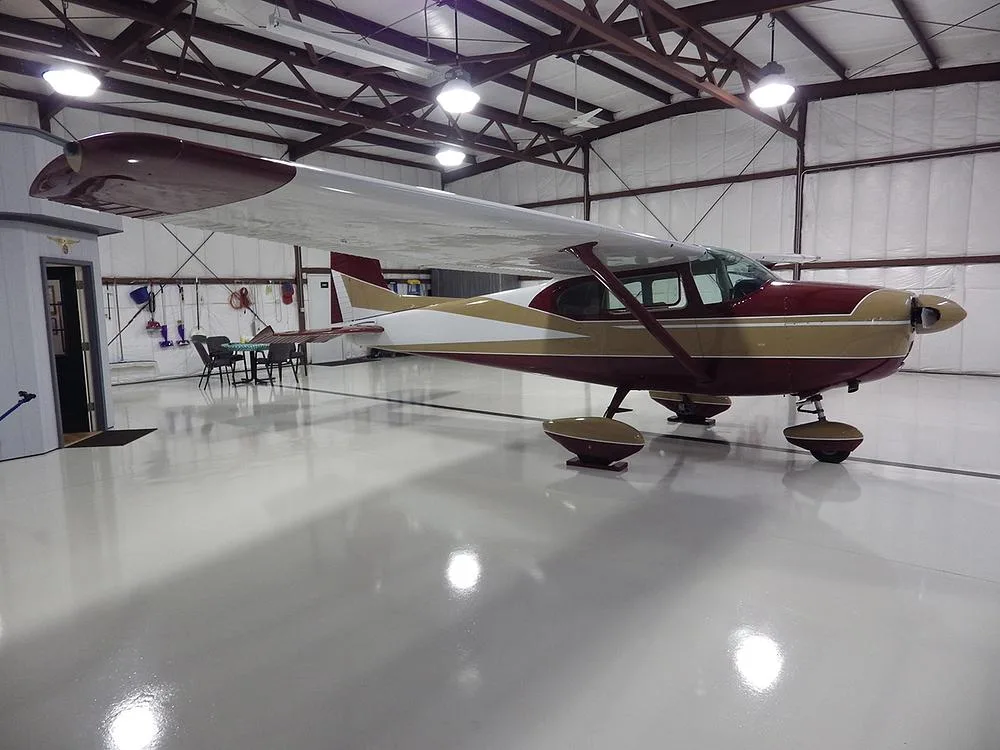 A red, gold, and white high-wing single-engine aircraft parked inside a well-lit hangar.