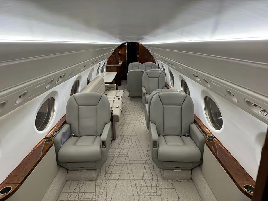 A view of the aircraft cabin from the front, showing light gray leather seats, a sofa, and wooden accents.