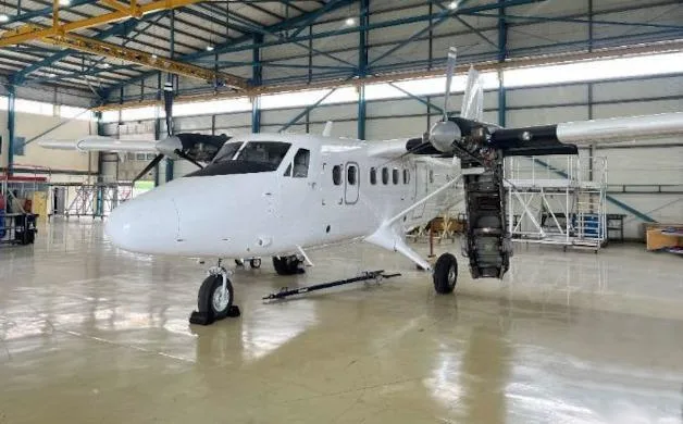 A white twin-engine turboprop aircraft is shown from the front-side in a hangar, with its right engine cowling open.